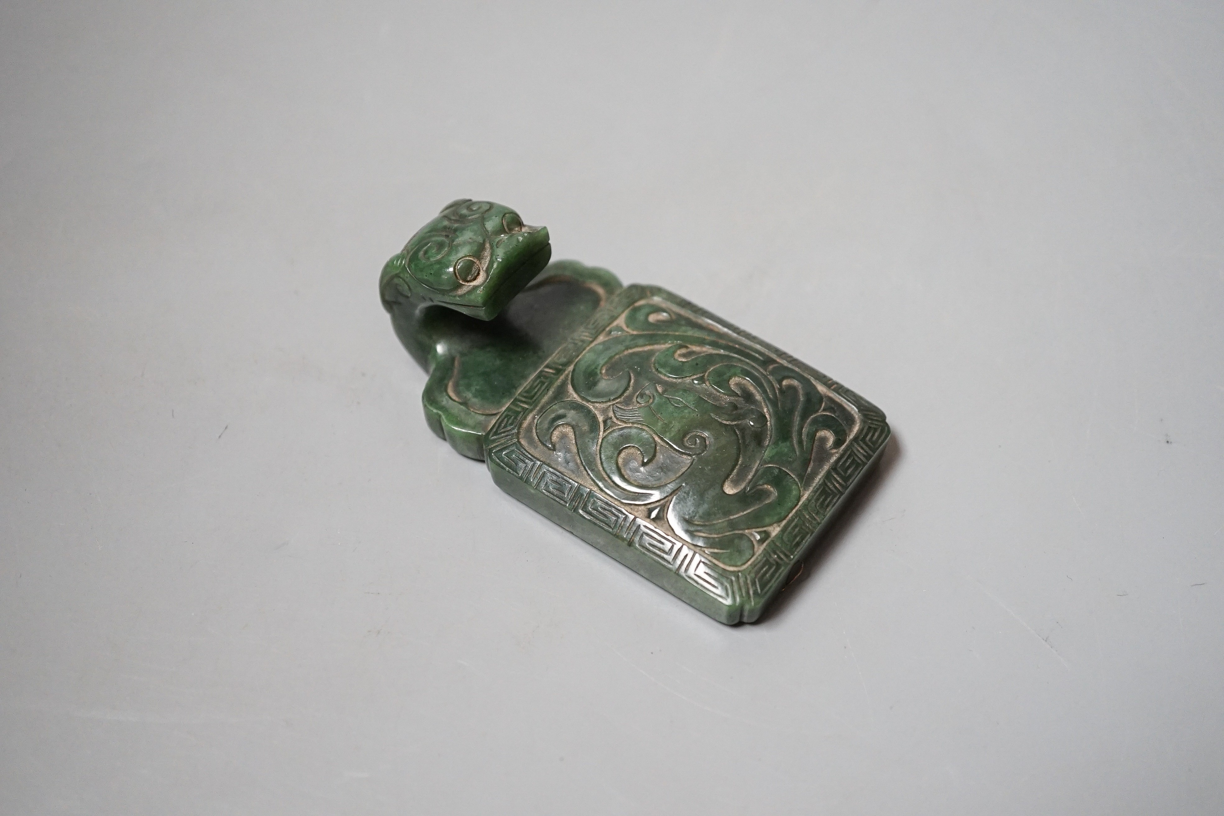 A Chinese spinach green jade belt hook, 19th century, in archaistic style, carved in relief with a chi-dragon, with a dragon head handle, 9cm